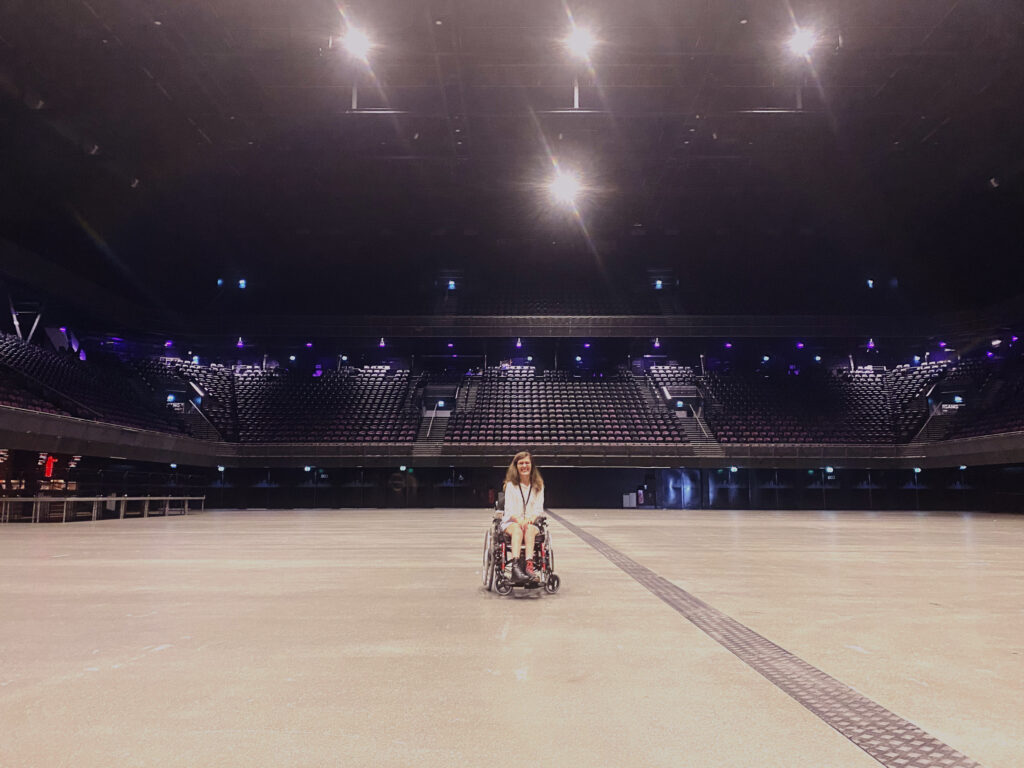 Maartje sits in her wheelchair in the center of a light up but empty Ziggo Dome.