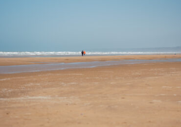 Two people walking in the distance on Omaha Beach in Normandy, France, on a sunny day.