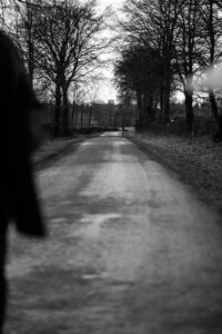 Black and white image photograph of a road with an out of focus foreground and a in focus background, nearing sunset
